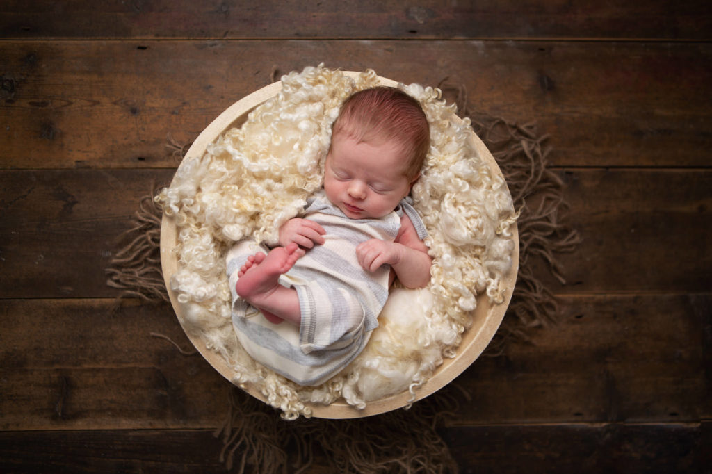 Newborn baby boy lying in a bowl with the wooden floor backdrop-Caerphilly Photographer