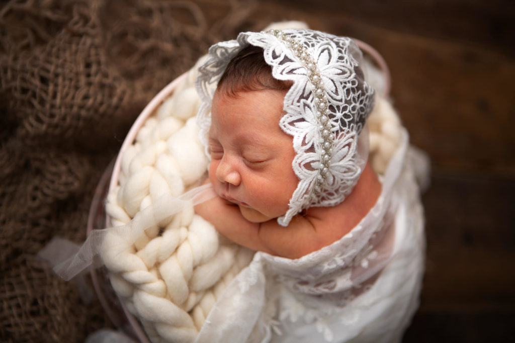 Newborn baby girl lying on her arms wearing a lace bonnet at her newborn session in Caerphilly