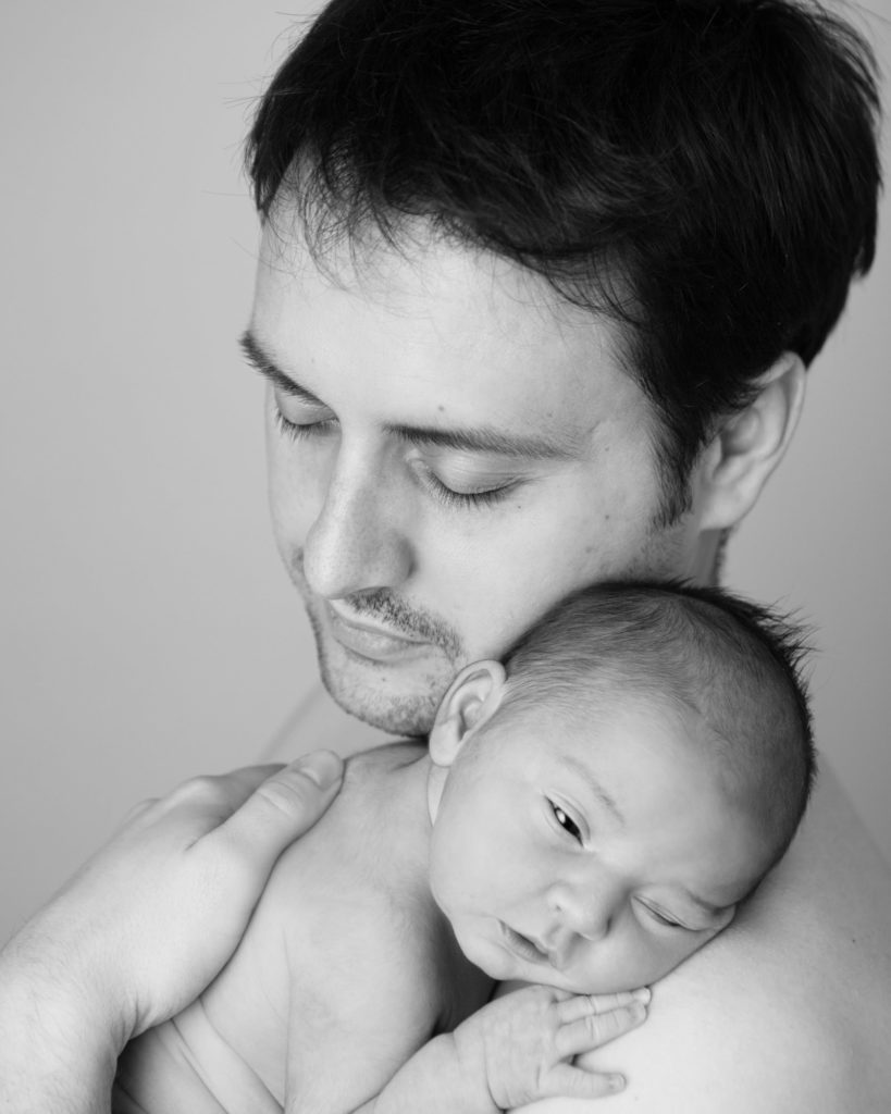 Father hold his newborn daughter in a black and white photo during their newborn session in Caerphilly