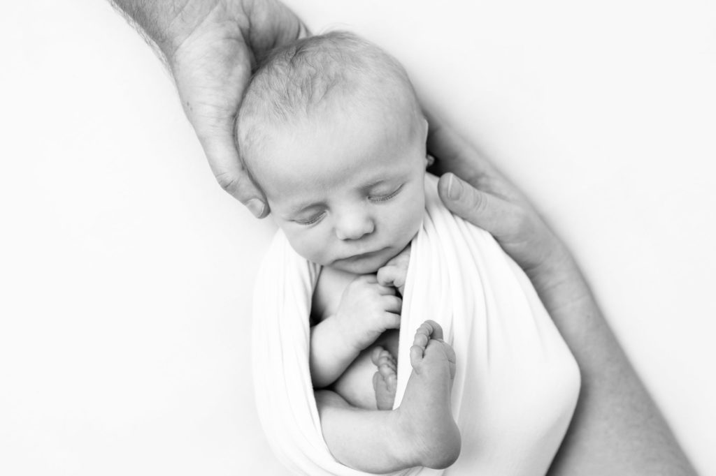 a black and white image of a baby wrapped up and his parents hands are holding him