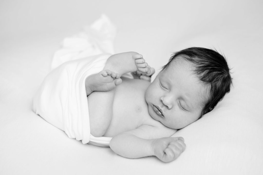 a newborn baby who is sleeping all curled up at a photoshoot in Caerphilly