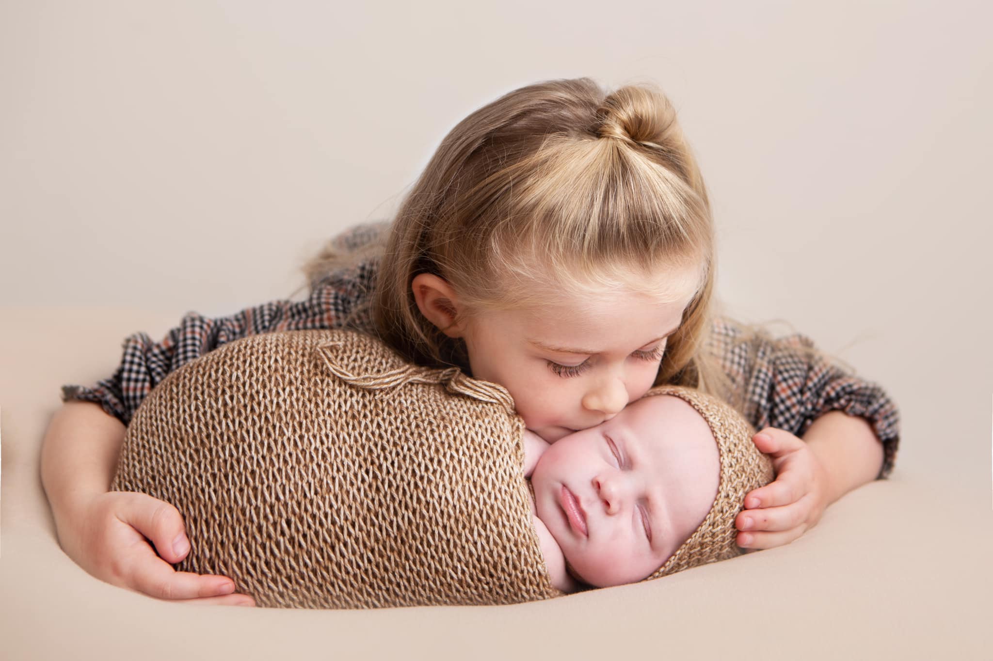 big sister kissing her brother who is wrapped in a brown wrap