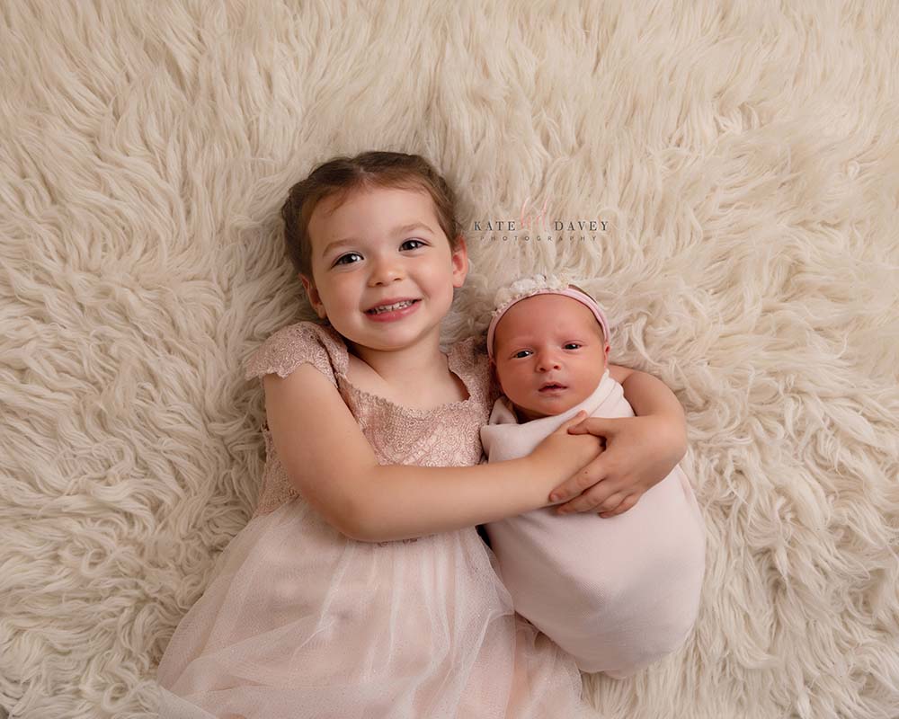 little girl wearing a pink dress holding her baby sister with a pink headband