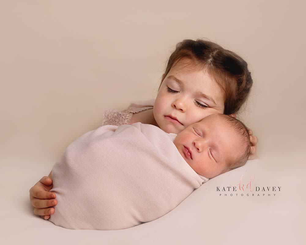 little girl cuddling her newborn baby sister